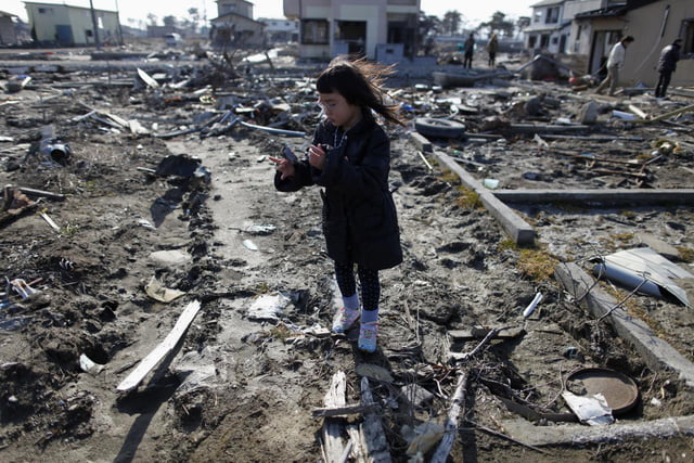 Một bé gái Nhật đứng trên đống đổ nát gây ra do trận động đất và sóng thần năm 2011 tại tỉnh Miyagi - Ảnh: REUTERS